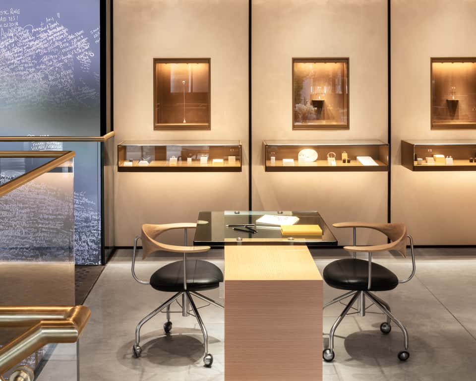 Inside the VASHI Covent Garden flagship store, a large digital screen showing the Love Wall installation, a desk and shelves with jewelry displays with wood accents.
