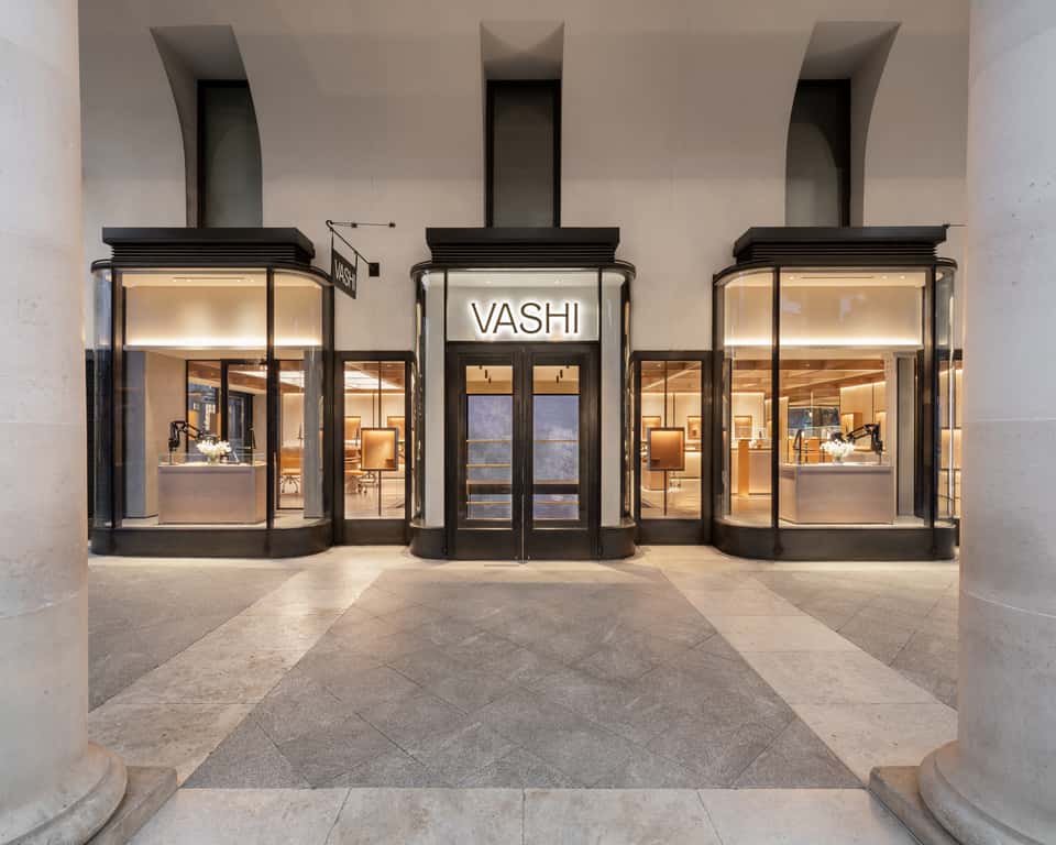 Storefront of Vashi jewelry shop with large glass windows and illuminated displays, and a huge illuminated screen behind the central entrance door.